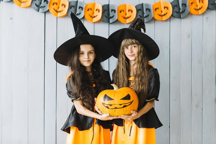 Two young witches holding a Halloween pumpkin