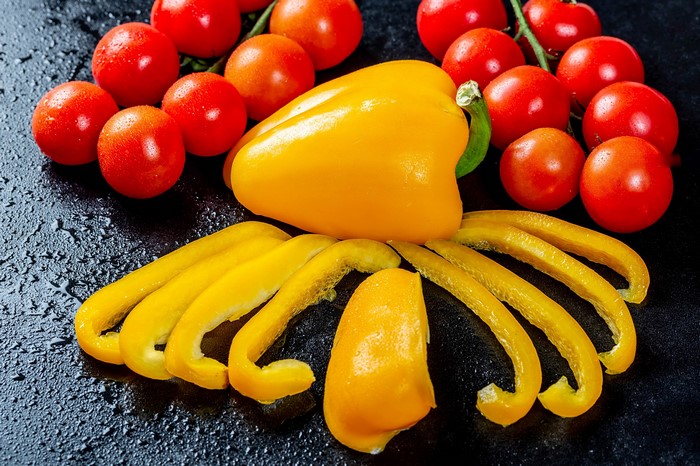 Yellow bell pepper and cherry tomatoes on a dark surface
