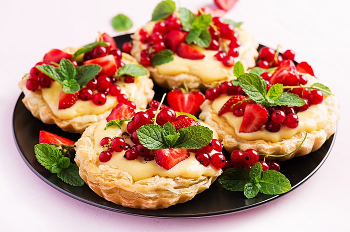 Mini tarts with custard, strawberries, and red currants on a plate