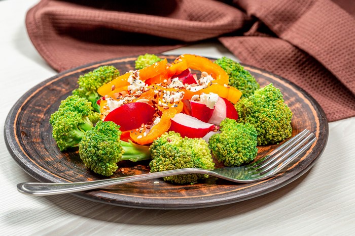 Salad with broccoli, radish, bell pepper, and cheese on a plate with a fork