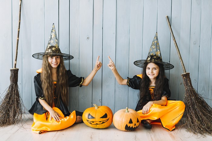 Two young girls dressed as witches with pumpkins and brooms