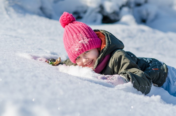 Girl in pink hat lying in snow