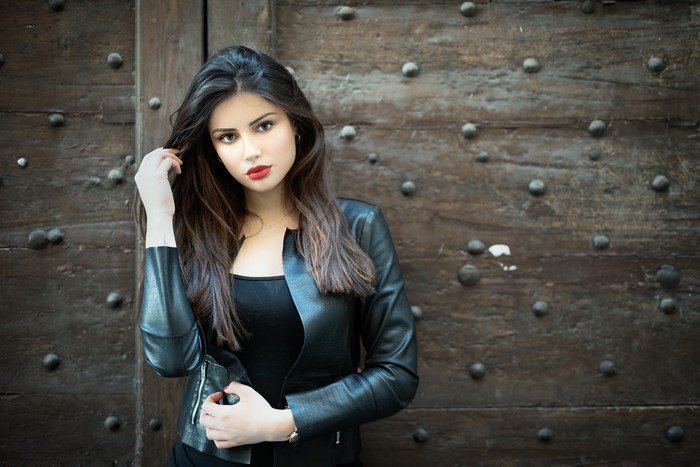 Brunette girl in leather jacket posing against wooden door