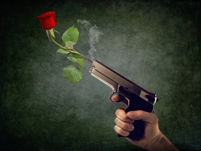 Hand holding a pistol with a rose emerging from the barrel