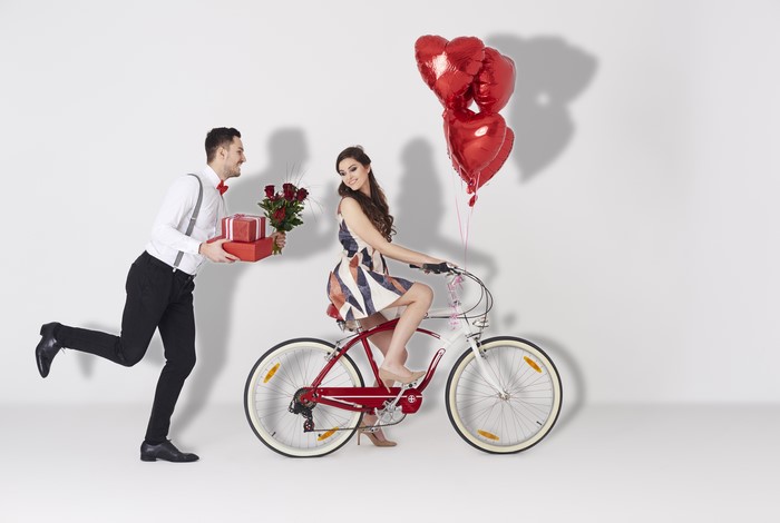 Man running with gifts and roses towards woman on bicycle with balloons