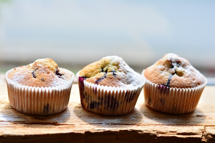 Three blueberry muffins with powdered sugar