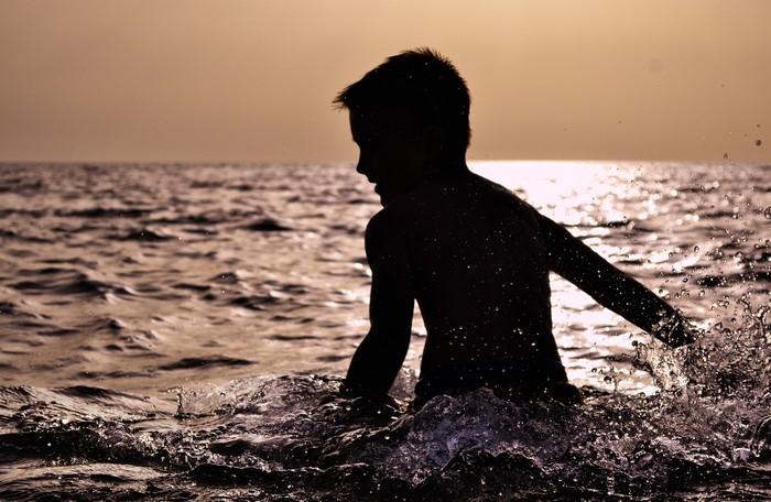 Silhouette of a boy splashing in the sea at sunset