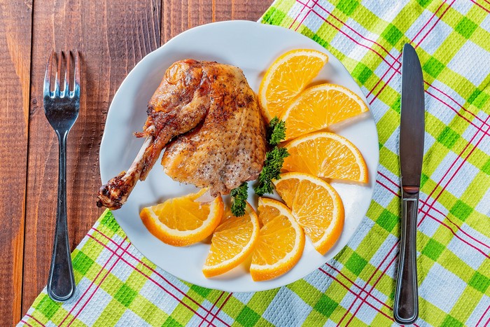 Roast chicken leg with orange slices on a plate