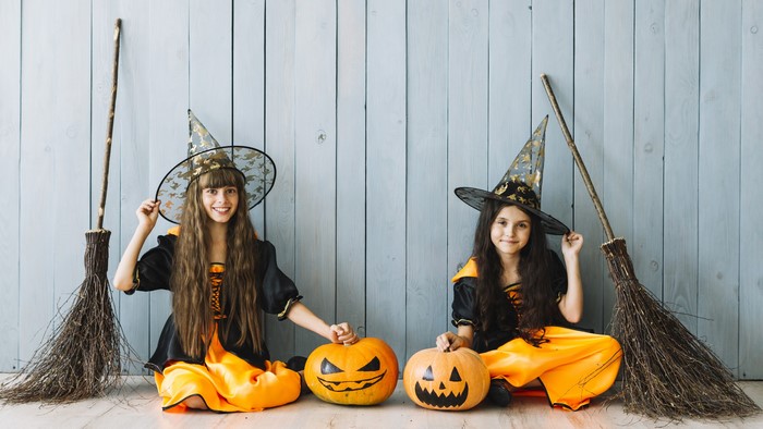 Two young girls dressed as witches with pumpkins and brooms