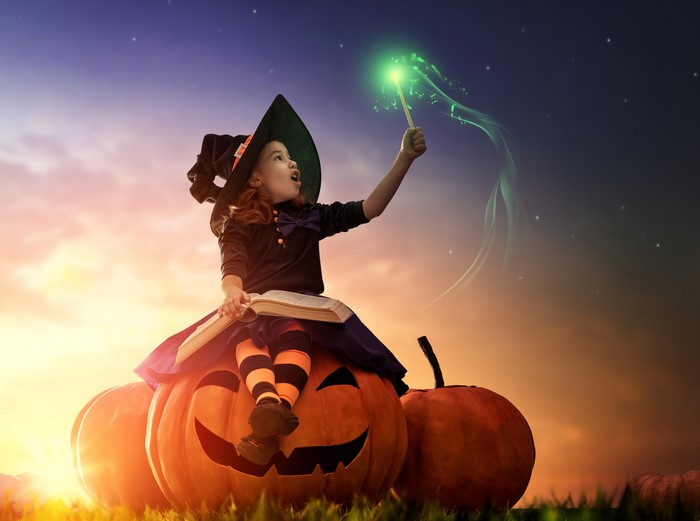 Little girl witch with magic wand on pumpkins