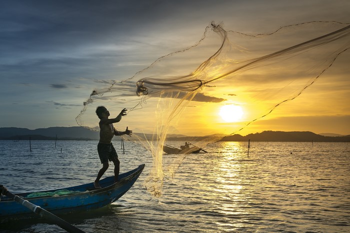 Man fishing with net from boat at sunset