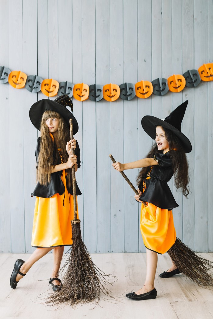 Two young girls dressed as witches holding brooms