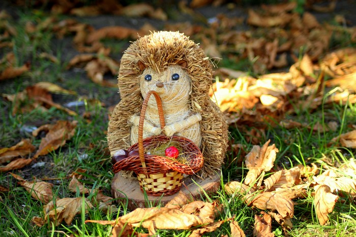 Straw hedgehog toy with basket in autumn leaves