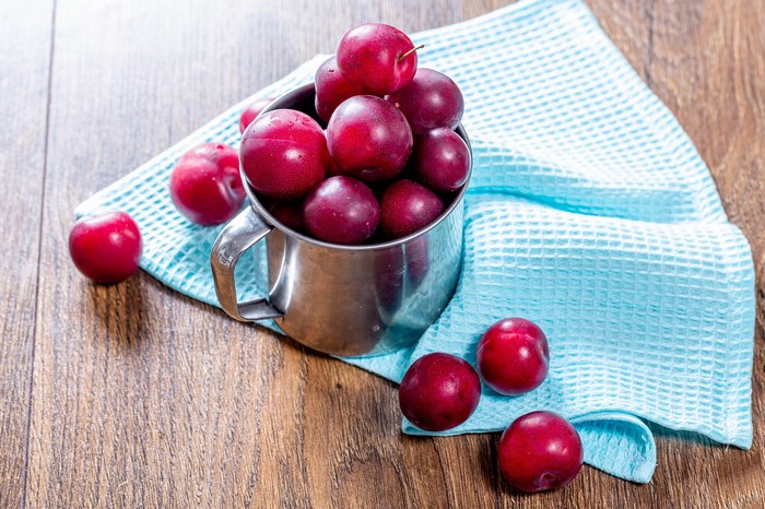Plums in a metal mug on a blue cloth