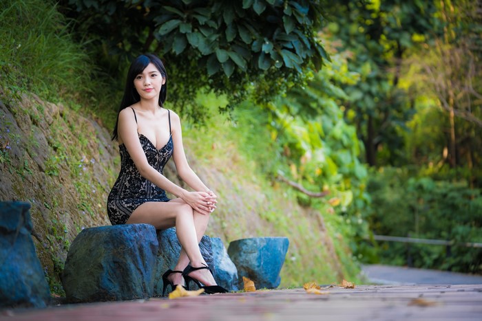 Asian woman in black dress sitting on stones