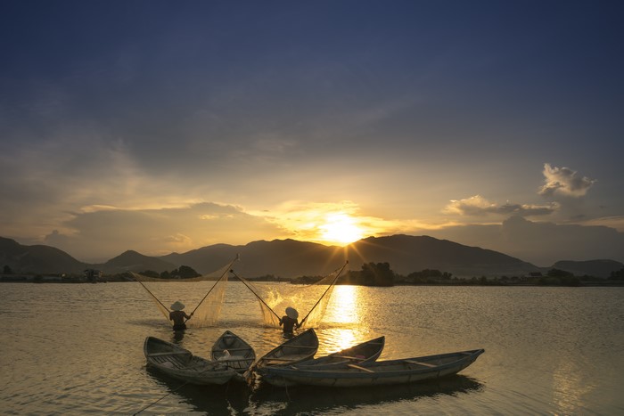 Fishermen casting nets at sunset with boats