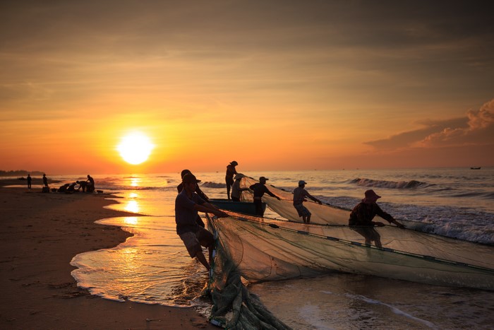 Fishermen pulling nets at sunrise on Asian coast