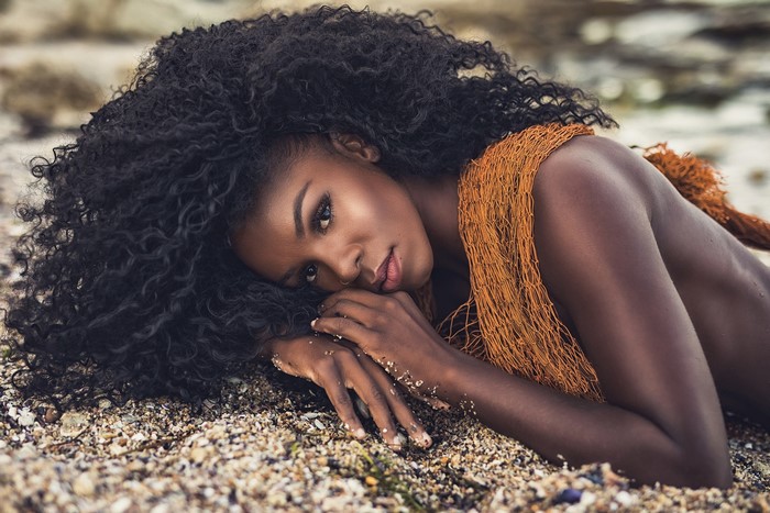 Curly Brunette Woman Lying on Pebble Beach