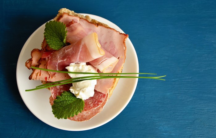 Open-faced sandwich with ham, sausage, and cheese on a plate