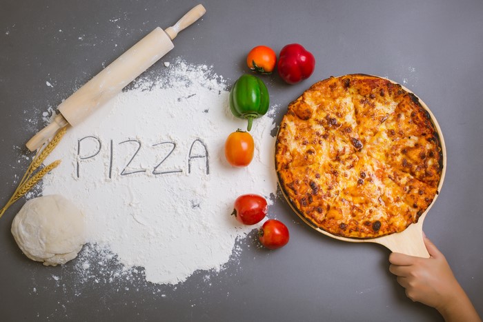 Pizza ingredients and a rolling pin with the word PIZZA written in flour