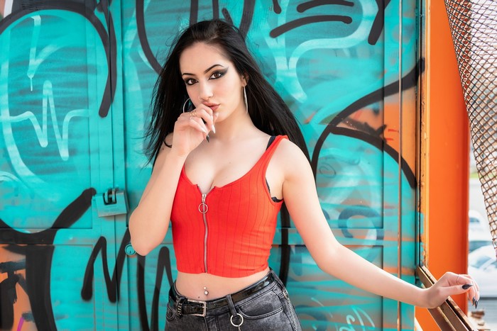 Brunette girl in red top posing against graffiti wall
