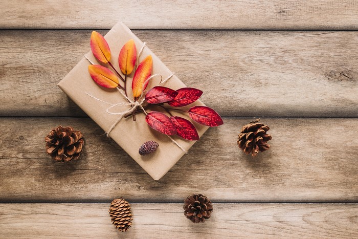 Gift wrapped in brown paper with autumn leaves and pine cones on wood