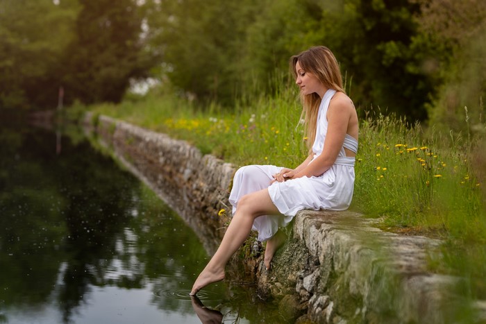 Woman in white dress sitting by a pond