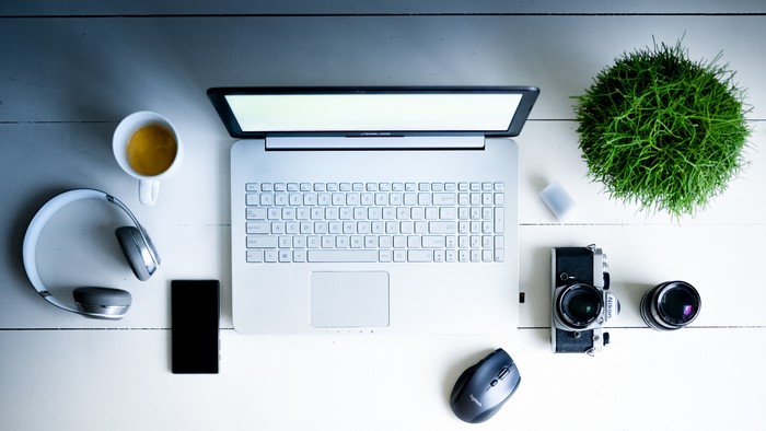 Laptop, headphones, coffee, smartphone, camera, and plant on desk