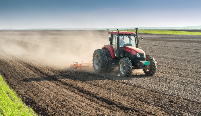 Red tractor plowing a dusty field