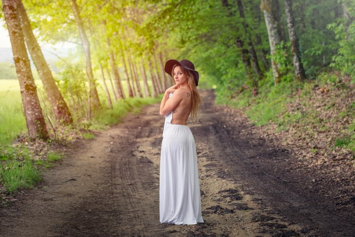 Woman in white dress and hat on forest road