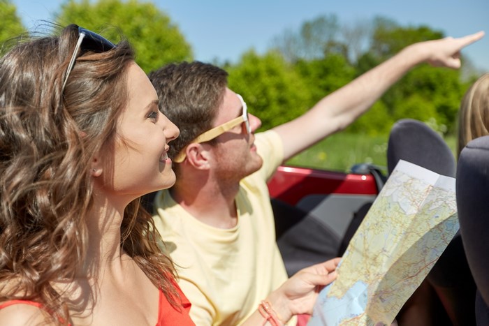 Couple in convertible with map and pointing