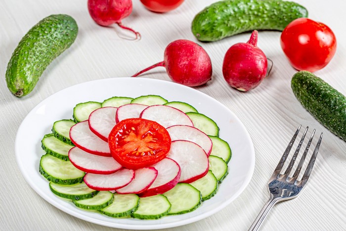 Sliced cucumbers, radishes, and tomato on a plate with fork