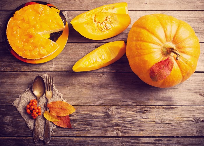Pumpkin pie with pumpkin slices and cutlery on wood