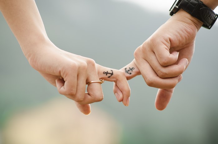 Two hands with anchor tattoos holding fingers