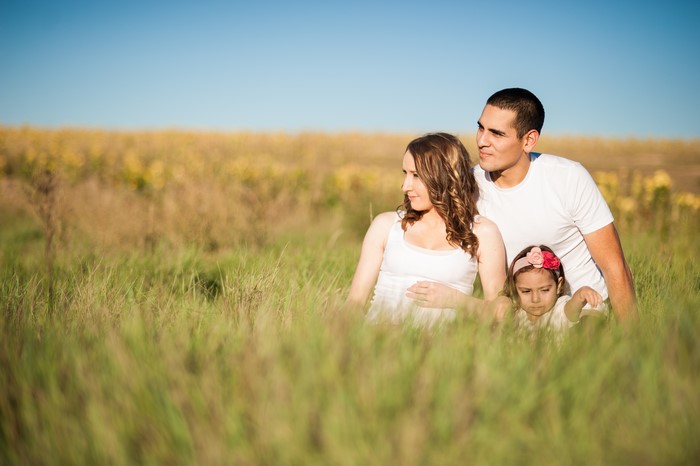 Family of three sitting in a grassy field