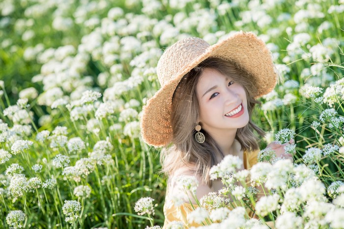 Asian woman in a straw hat smiling in a field of white flowers