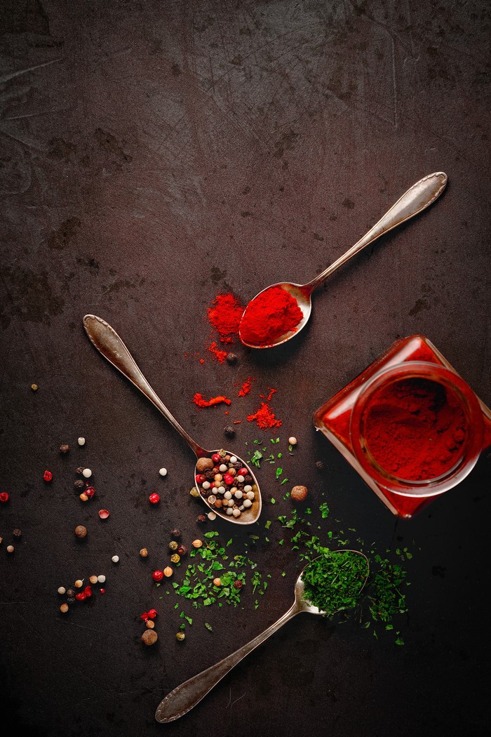 Spoons with spices and herbs on a dark surface