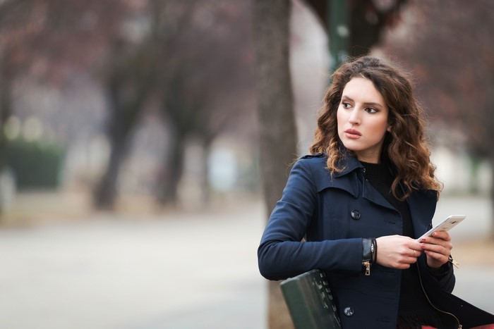 Woman with brown hair holding a smartphone on a bench