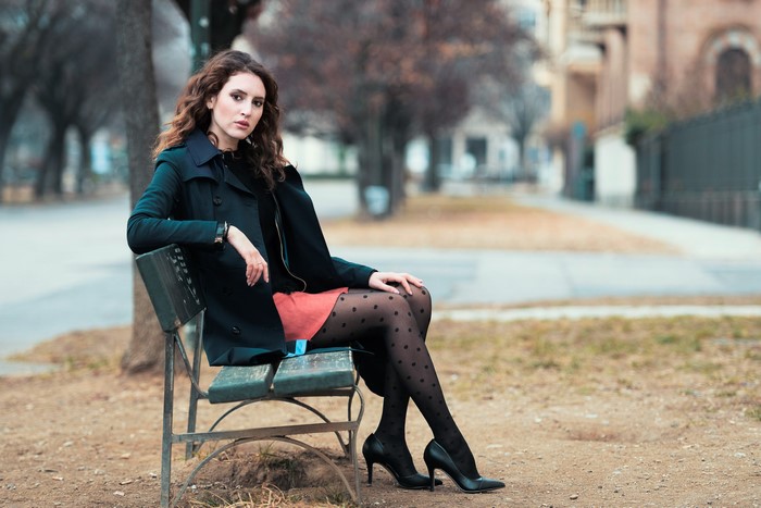 Woman in coat and polka dot tights sitting on a bench