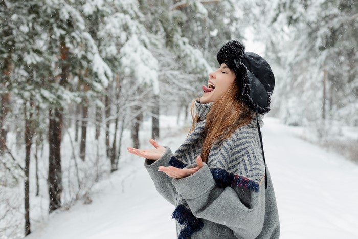 Woman in winter hat catching snow on her tongue