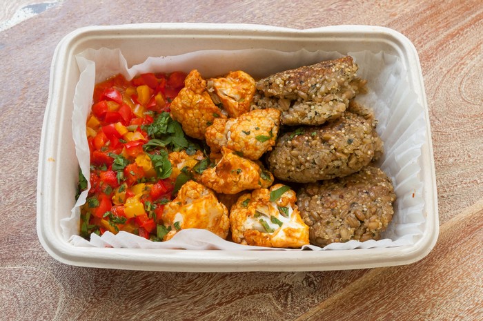 Takeout container with cauliflower, peppers, and patties