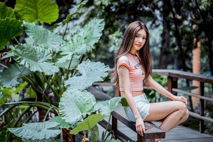 Asian woman sitting on a wooden bench near foliage