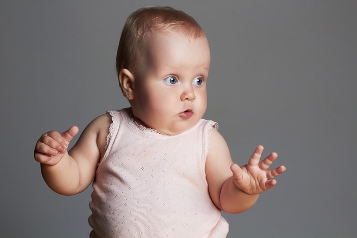Infant with hands up on gray background