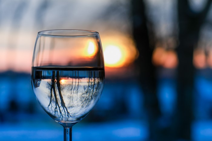 Glass of water reflecting sunset and trees