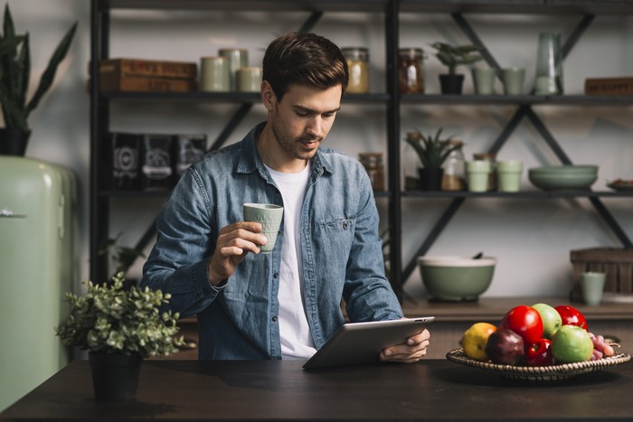 Man holding cup and tablet in kitchen