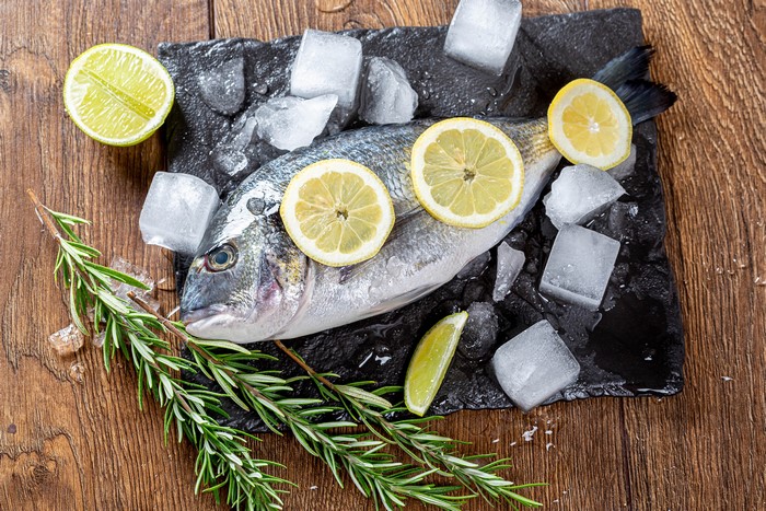 Fresh fish with lemon slices and rosemary on ice