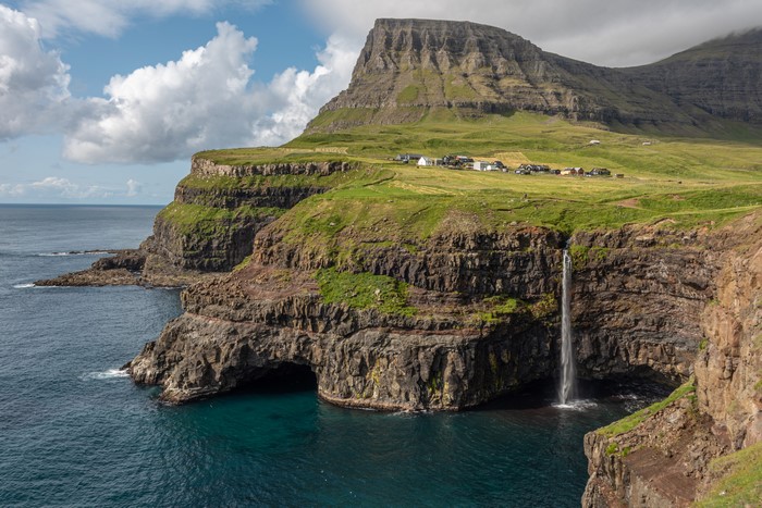 Waterfall cascading from cliffs into the sea near a village in the Faroe Islands