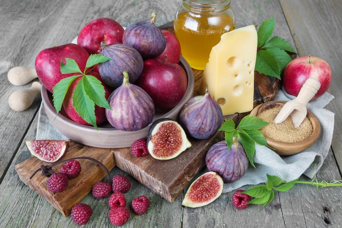 Apples, figs, raspberries, cheese, and honey on a wooden table