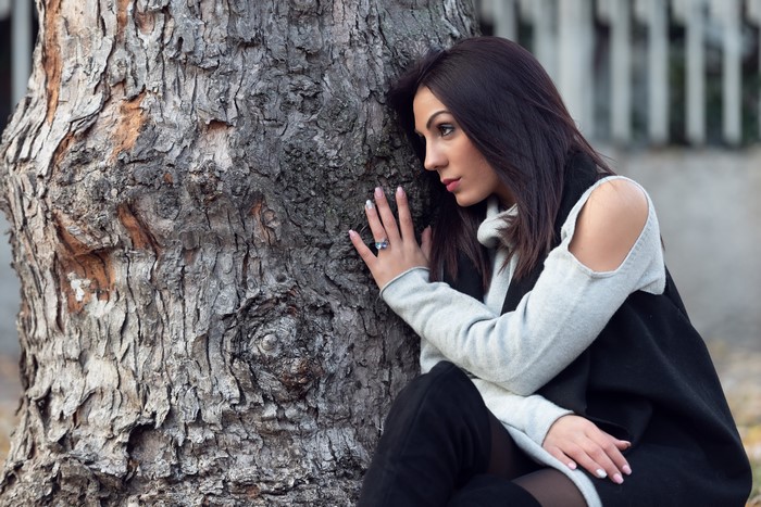 Brunette girl leaning on a tree trunk