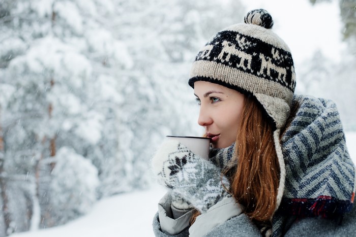 Woman in Winter Hat Drinking from Mug in Snow